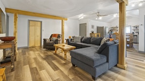 Un amplio espacio de estar con piso de madera, un sofá gris, una mesa de centro de madera y una mesa de comedor con sillas.