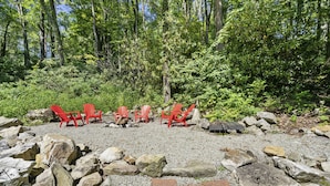Un área boscosa con sillas Adirondack rojas dispuestas sobre grava, rodeada de grandes rocas y árboles.