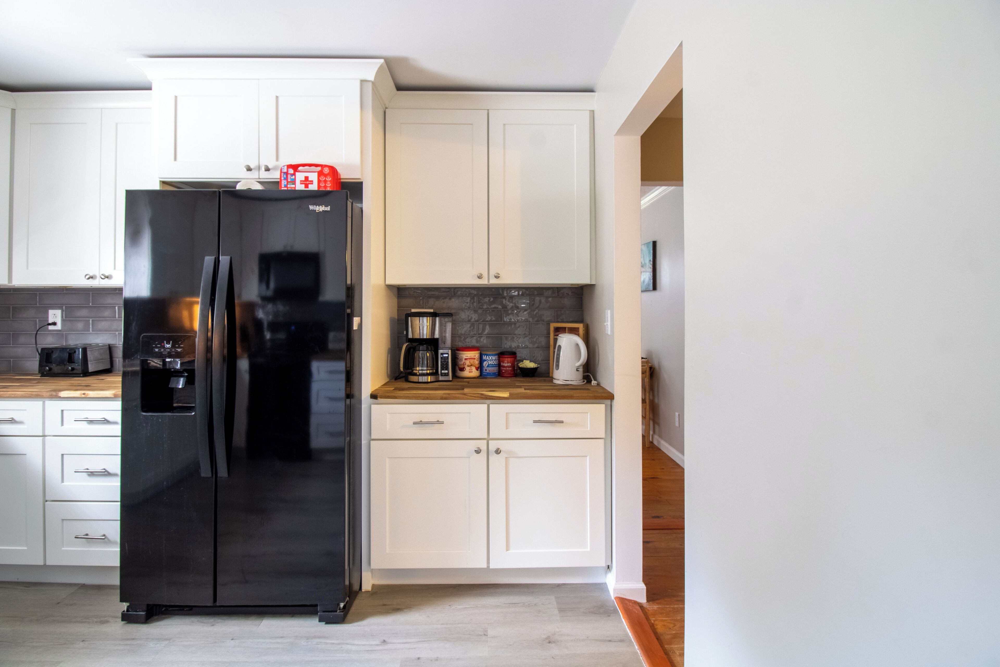 A modern kitchen with white cabinets, a black refrigerator, and a wooden countertop.