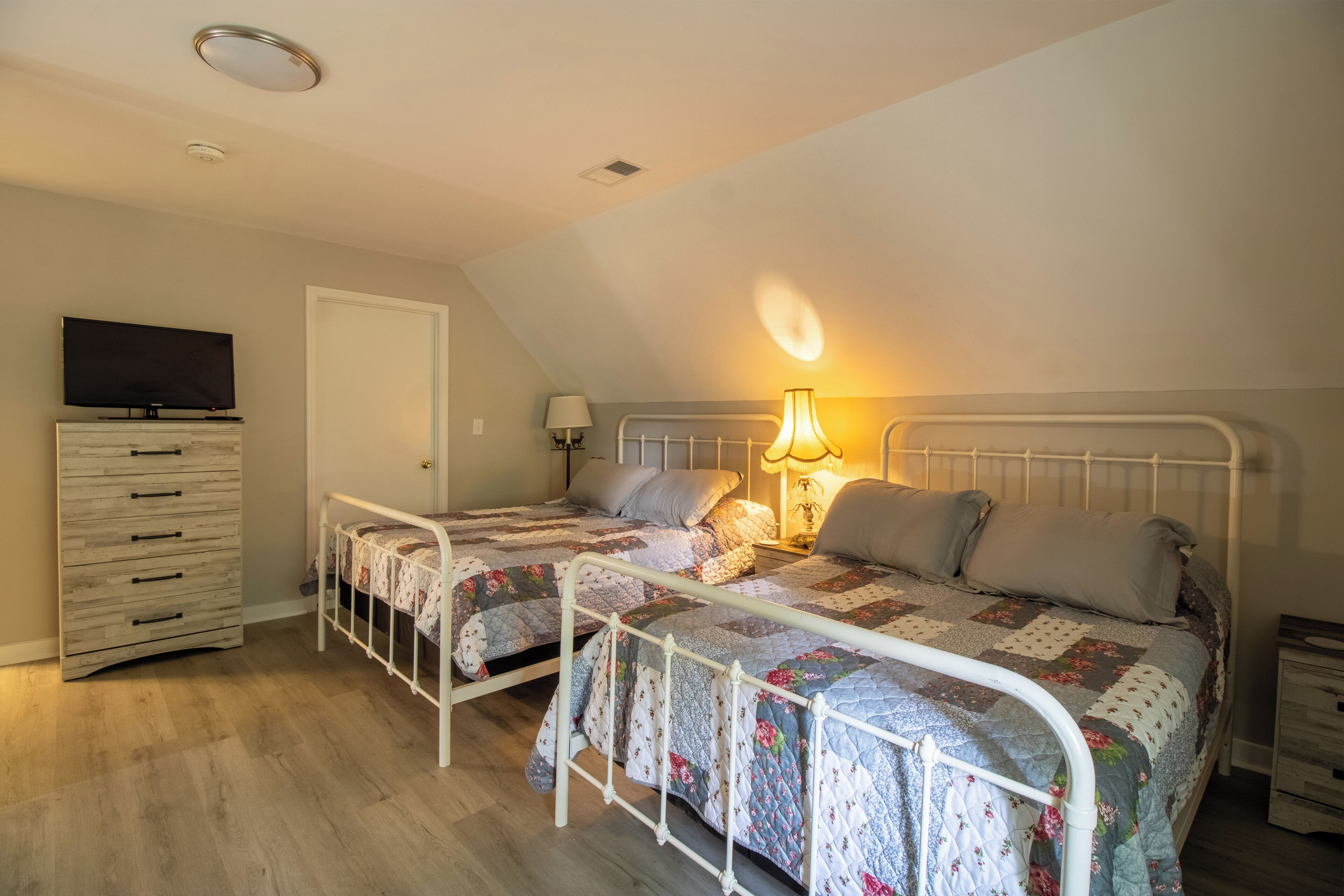 A bedroom with two beds, a TV, a dresser, and a lamp.