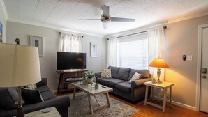 Ein Wohnzimmer mit einer Couch, einem Couchtisch, einem Fernseher und einem Deckenventilator.