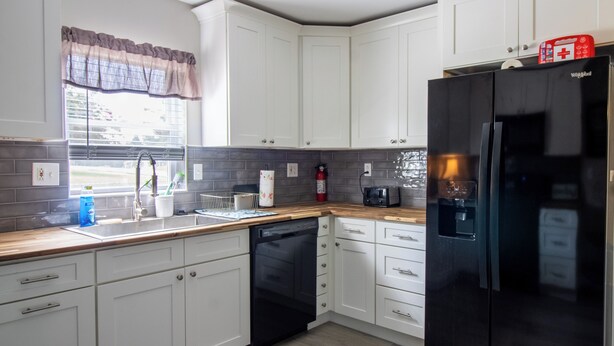 Eine moderne Küche mit weißen Schränken, einem schwarzen Kühlschrank und einer Holz Arbeitsplatte.