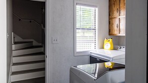 Ein Waschbereich mit Waschmaschine und Trockner, ein Fenster mit Jalousien sowie ein Holzkabinett.