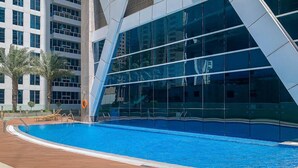 Un edificio moderno con facciata in vetro riflettente e area piscina con pavimento in legno e poltrone relax.