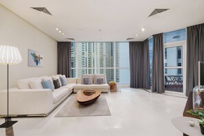 A modern living room with a sofa, a wooden coffee table, and a large window with curtains. - Maison Privee - Urban Apt in Dubai Marina w/ Partial Sea Views (Dubai)
