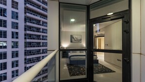 Una camera d'albergo moderna con una porta in vetro, un letto, un quadro appeso al muro e vista su un grattacielo.