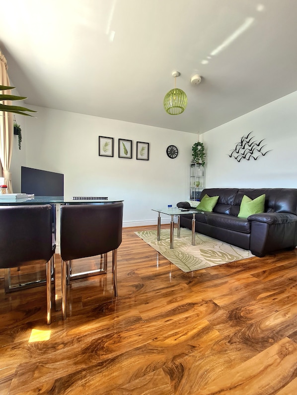 A modern living room with a dark leather sofa, a glass coffee table, and a dining area with a dark table and chairs. - Stylish Coastal Stay with Mountain Views for couple/solos & dogs - walk to beach (Prestatyn)