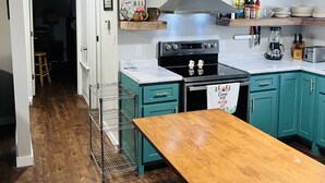 Une cuisine avec des armoires de couleur turquoise, une table en bois et une hotte de cuisinière en acier inoxydable.