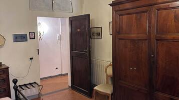 A bedroom with a bed, a wooden wardrobe, a chair, a chandelier, and a door leading to another room.