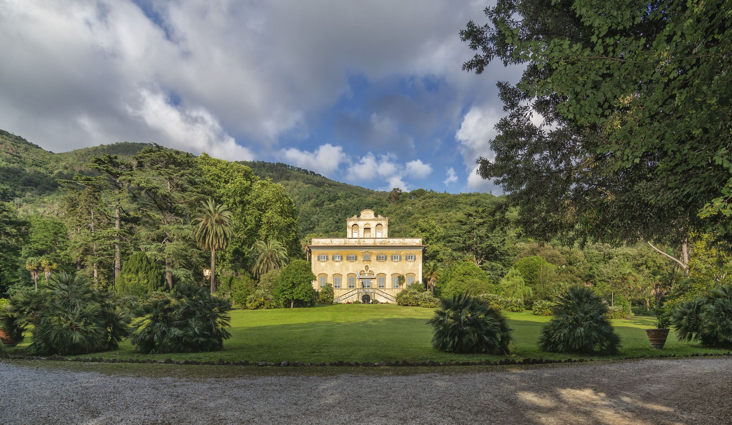 A large, historic building with a symmetrical facade, surrounded by lush greenery and a well-maintained lawn.
