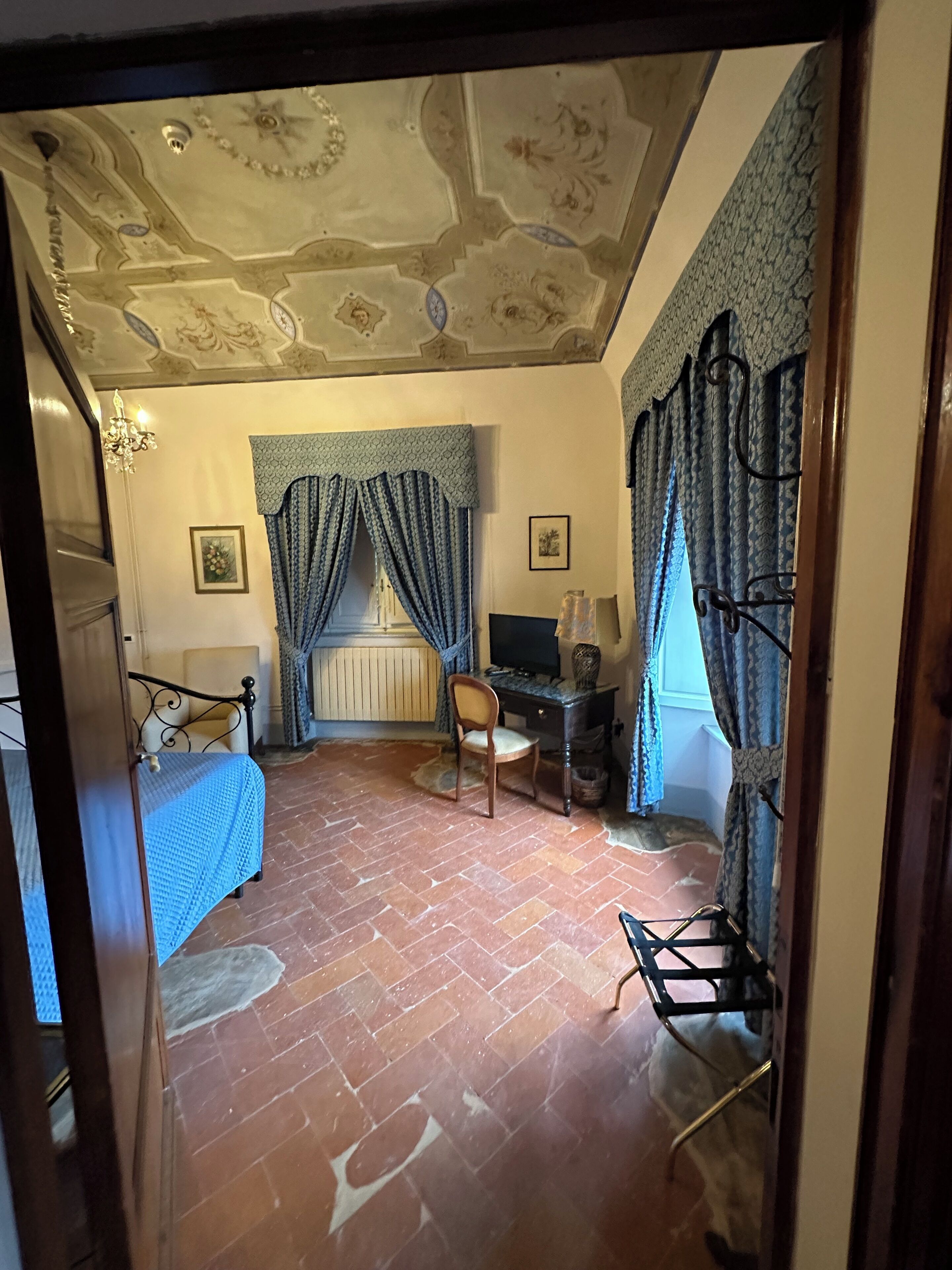 A bedroom with a bed, a desk, a chair, a radiator, and a television.