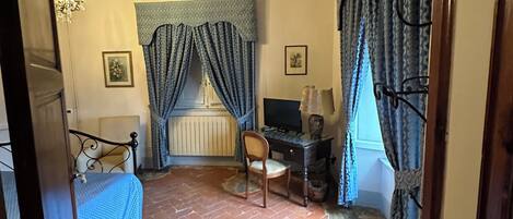 A bedroom with a bed, a desk, a chair, a radiator, and a television.