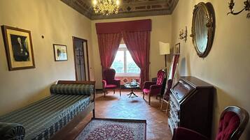 Une pièce avec un tapis à motifs, un canapé, un fauteuil rouge, un miroir et un lustre.