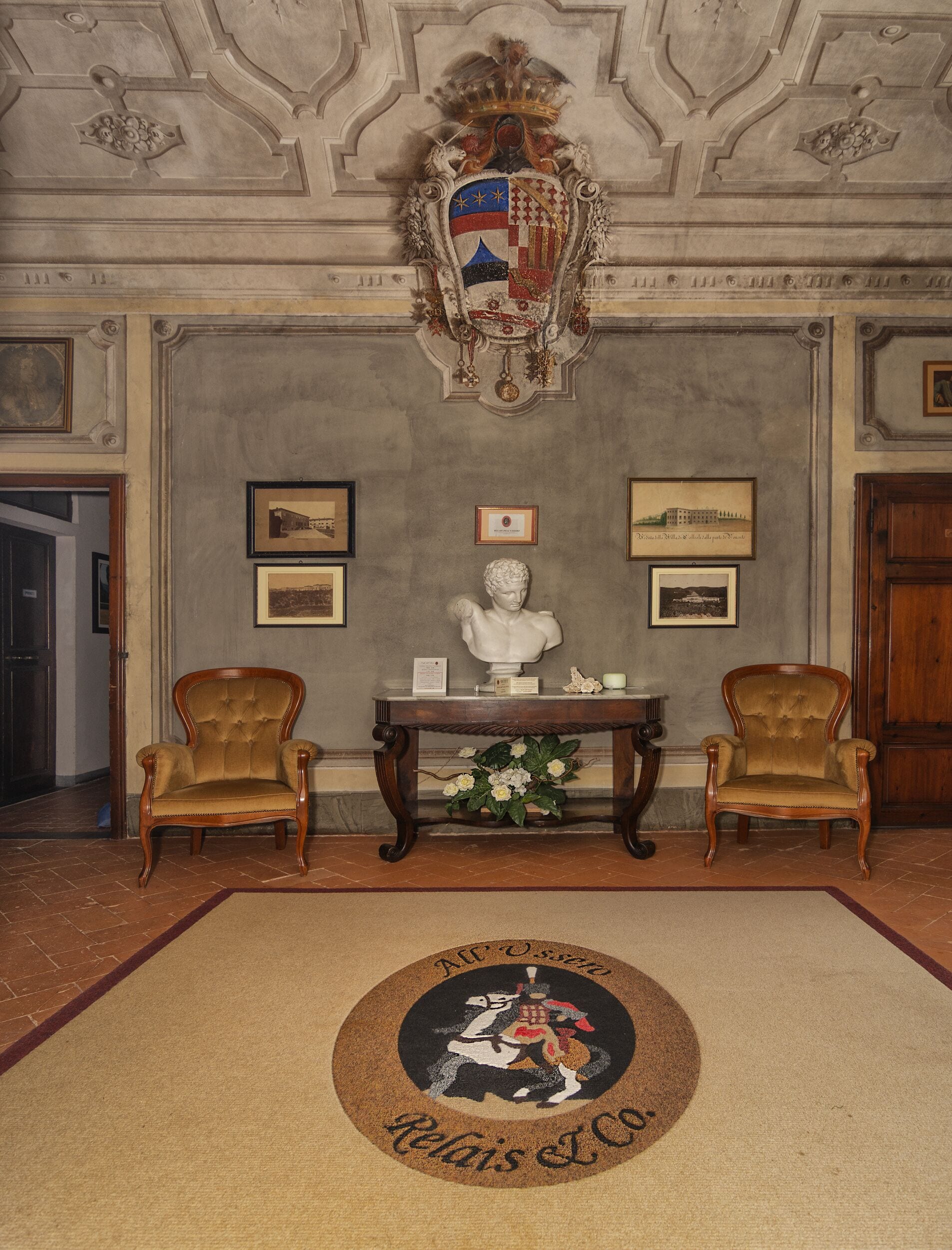 Une pièce élégante, dotée de deux fauteuils rembourrés, d’un buste sculpté, de tableaux encadrés et d’un motif décoratif ornant le plafond.