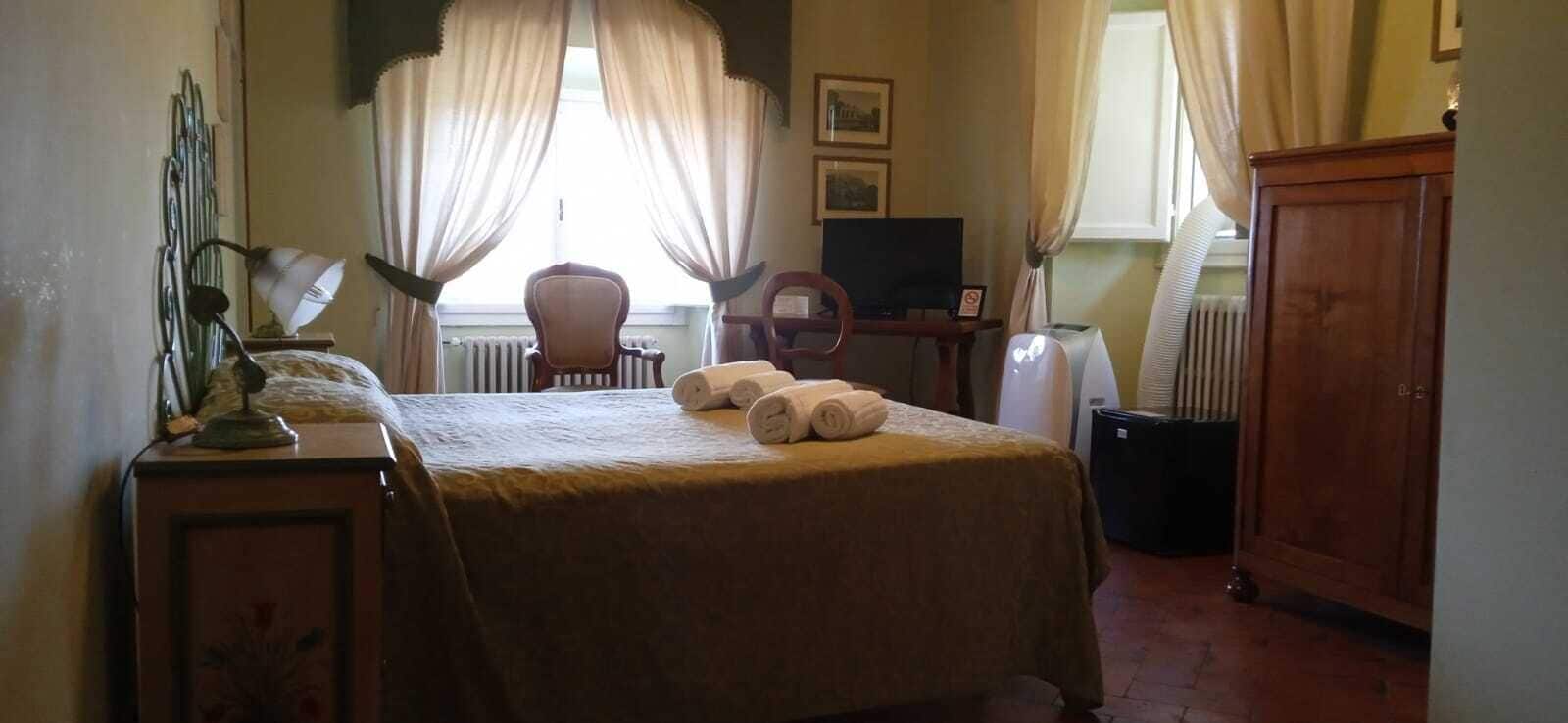A hotel room with a bed, a desk with a lamp, a chair, a television, and a radiator.