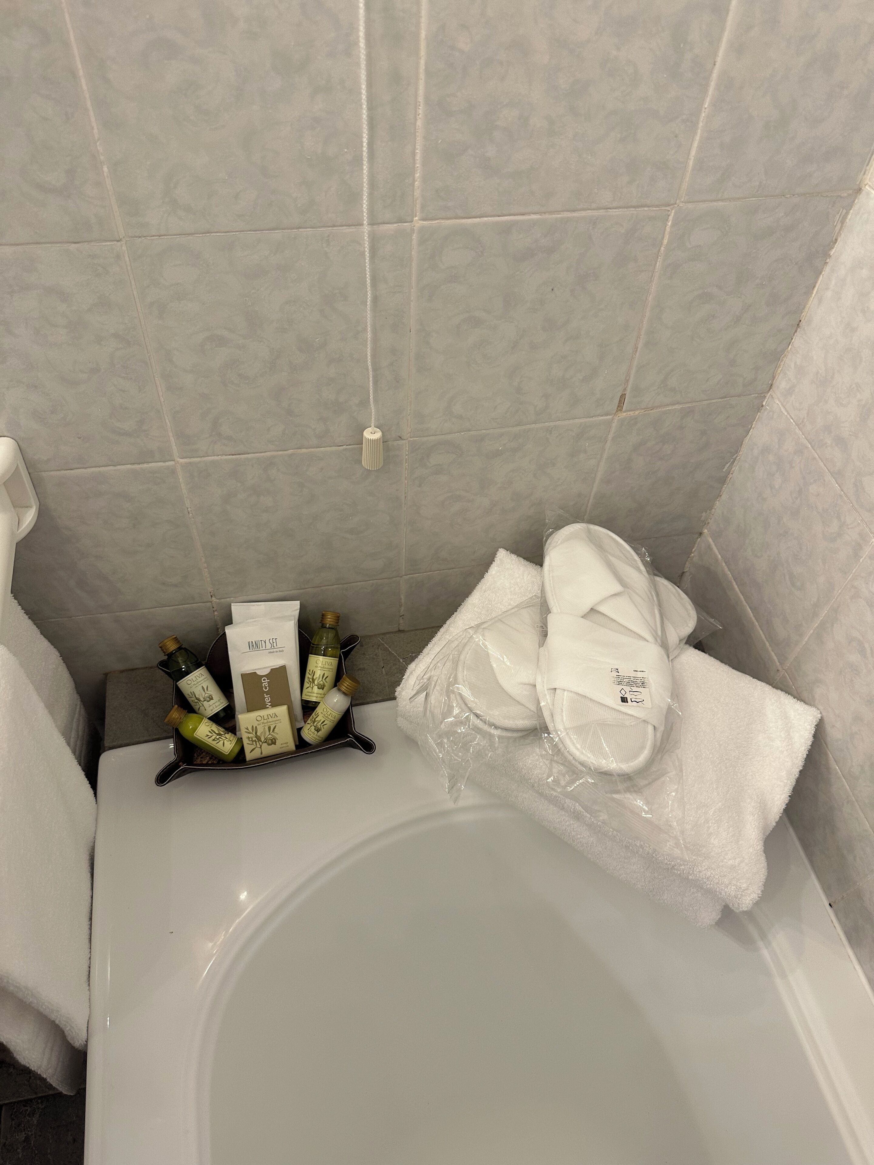 Un baño con bañera, un perchero con una toalla blanca y una bandeja con artículos de aseo.