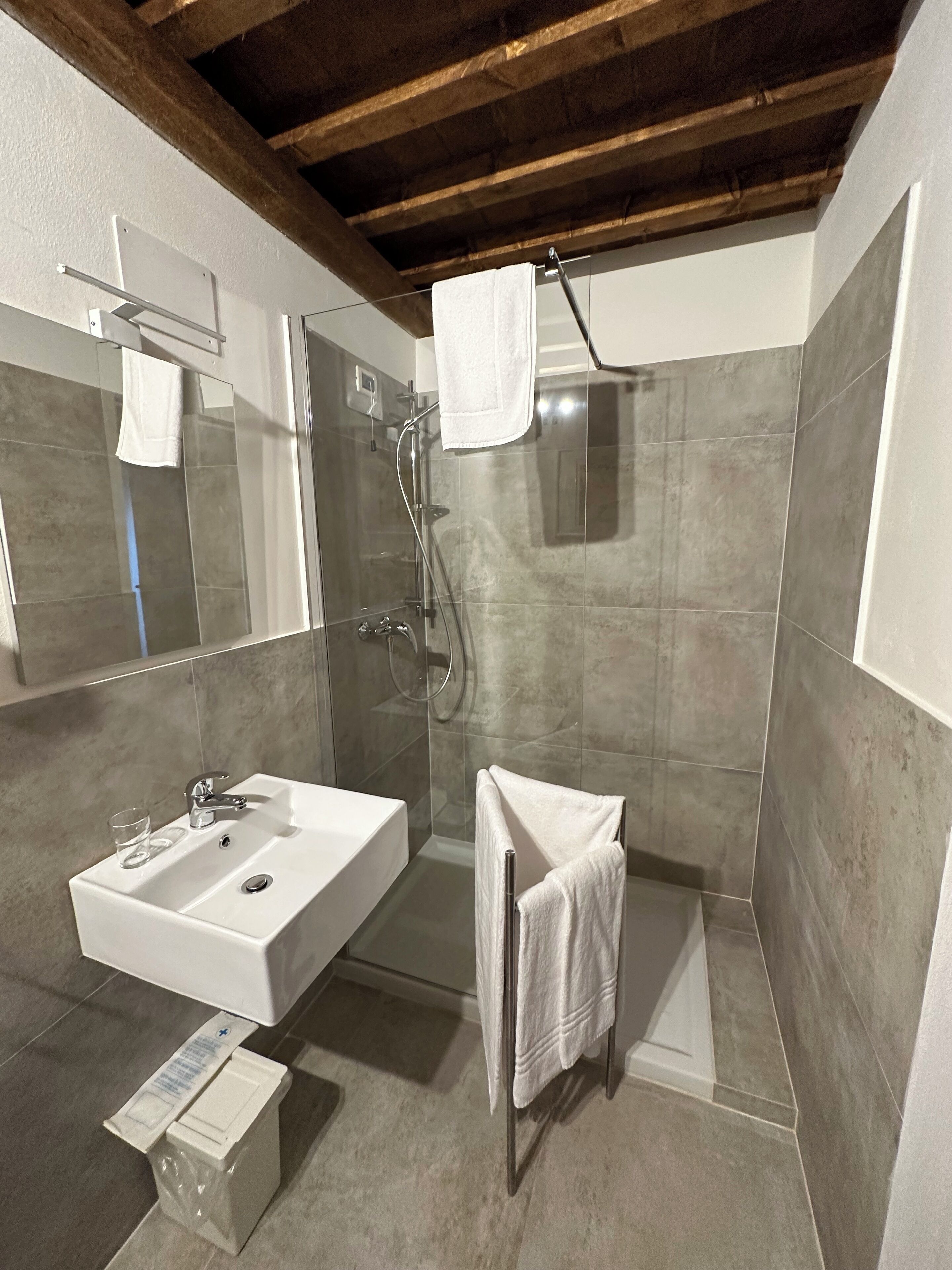 Ein modernes Badezimmer mit großem Spiegel, Waschbecken in Weiß, Duschkabine aus Glas und Handtuchhalter.