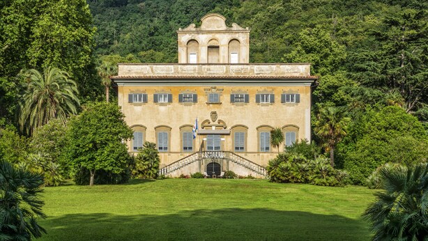 A large, historic building with a central staircase, surrounded by lush greenery and a hilly backdrop. - Relais all'Ussero a Villa di Corliano (San Giuliano Terme)