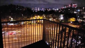 Vista nocturna desde un balcón con barandilla de metal, que da a un paisaje urbano con edificios y farolas.