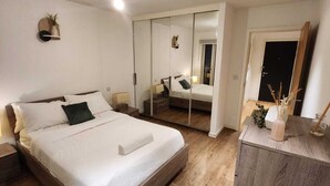 Un dormitorio moderno con cama de madera, mesita de noche, tocador, espejo y armario.