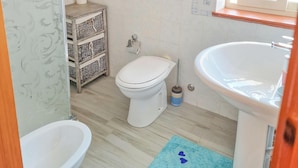 A bathroom with a toilet, bidet, and sink. There is a blue rug on the floor and a basket of toiletries.