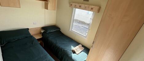 Un dormitorio de autocaravana compacto con dos camas, un ventanal y armarios de madera.
