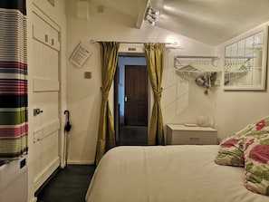 Quarto de hotel com cama, mesa de cabeceira, cabideiro e porta com cortina listrada.