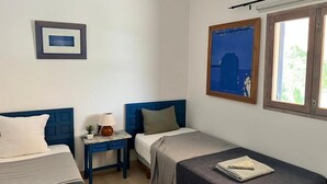 Une chambre avec deux lits, une petite table avec une lampe, un tableau encadré au mur et une fenêtre donnant sur un paysage.