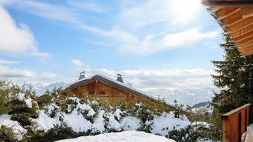 Une cabane en bois, dotée d’un toit en pente, entourée d’arbres couverts de neige et avec des montagnes en arrière-plan.