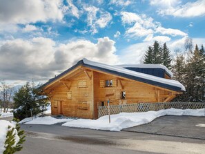 Una cabaña de madera con techo inclinado, rodeada de nieve y árboles.