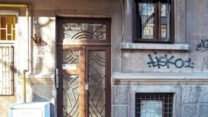 Facciata di un edificio con una porta doppia, una finestra con sbarre di metallo e graffiti sul muro.
