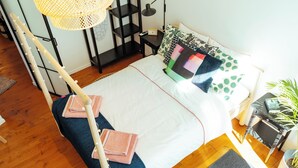 Un letto rifatto con cura, coperto da una trapunta bianca e blu, con numerosi cuscini e un comodino con lampada e libro.