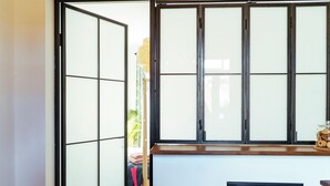 Una stanza con una porta scorrevole in vetro che dà su uno spazio esterno, un piccolo sgabello di legno e un armadietto nero.