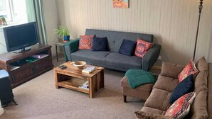 A living room with a grey sofa, a wooden coffee table, a television on a wooden stand, and a floor lamp.