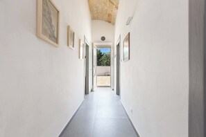 A hallway with a tiled floor, framed artwork on the walls, and a view of an outdoor area with trees.