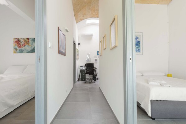 A hotel corridor with two beds on either side, a desk with a chair, and artwork on the walls.