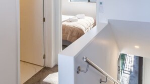 Una escalera moderna con barandilla que lleva a un dormitorio con cama y ventana.