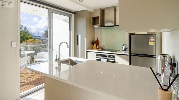 Una cocina moderna con una isla grande, electrodomésticos de acero inoxidable y una puerta corrediza de vidrio que da a un patio exterior.