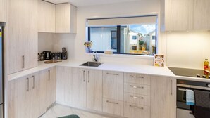 A modern kitchen with light wood cabinets, a white countertop, a built-in oven, and a window above the sink.