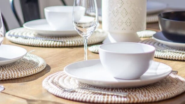 Una mesa de comedor dispuesta con platos, tazones y un vaso de agua, con un jarrón de tulipanes blancos en el centro.