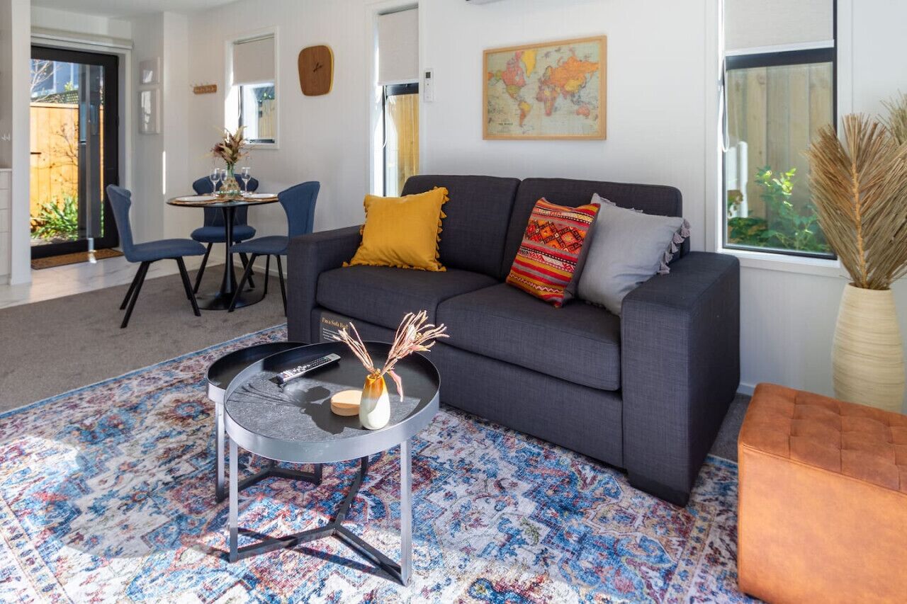 Ein modernes Wohnzimmer mit einem grauen Sofa, blauen Sesseln, einem runden Couchtisch und einem gemusterten Teppich.