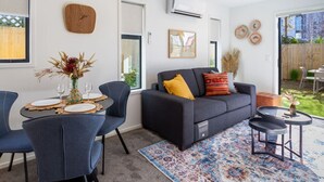 Una sala moderna con un sofá, sillas, una mesa de comedor preparada para cuatro personas y una alfombra estampada.