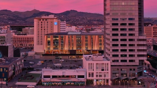 Un paisaje urbano con un edificio destacado identificado como 'CROWE PLAZA' y otro edificio alto de diseño moderno.
