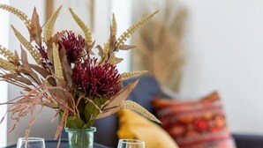 Una mesa de comedor con un florero de flores secas, dos copas de vino y platos preparados para una comida.
