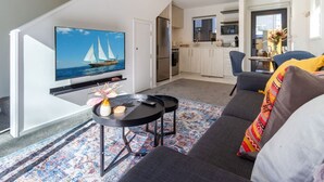 Una sala de estar moderna con un televisor de pantalla plana, un sofá, una mesa de centro y una cocina al fondo.