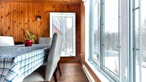 A cozy cabin interior with a wooden ceiling, a dining table with a plaid tablecloth, a red vase, and a chair. - Chalet in a dark sky reserve (Val-Racine)