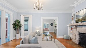 A spacious living room with a grey sofa, a chandelier, a fireplace, and a view into the dining area. - Charming Vintage 1BR, 1BA Apartment in Midtown @Piedmont Park. (Atlanta)
