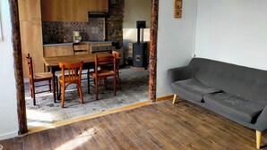 Un salon chaleureux avec une table et des chaises en bois, un canapé gris et un mur en pierre agrémenté d’une cheminée.