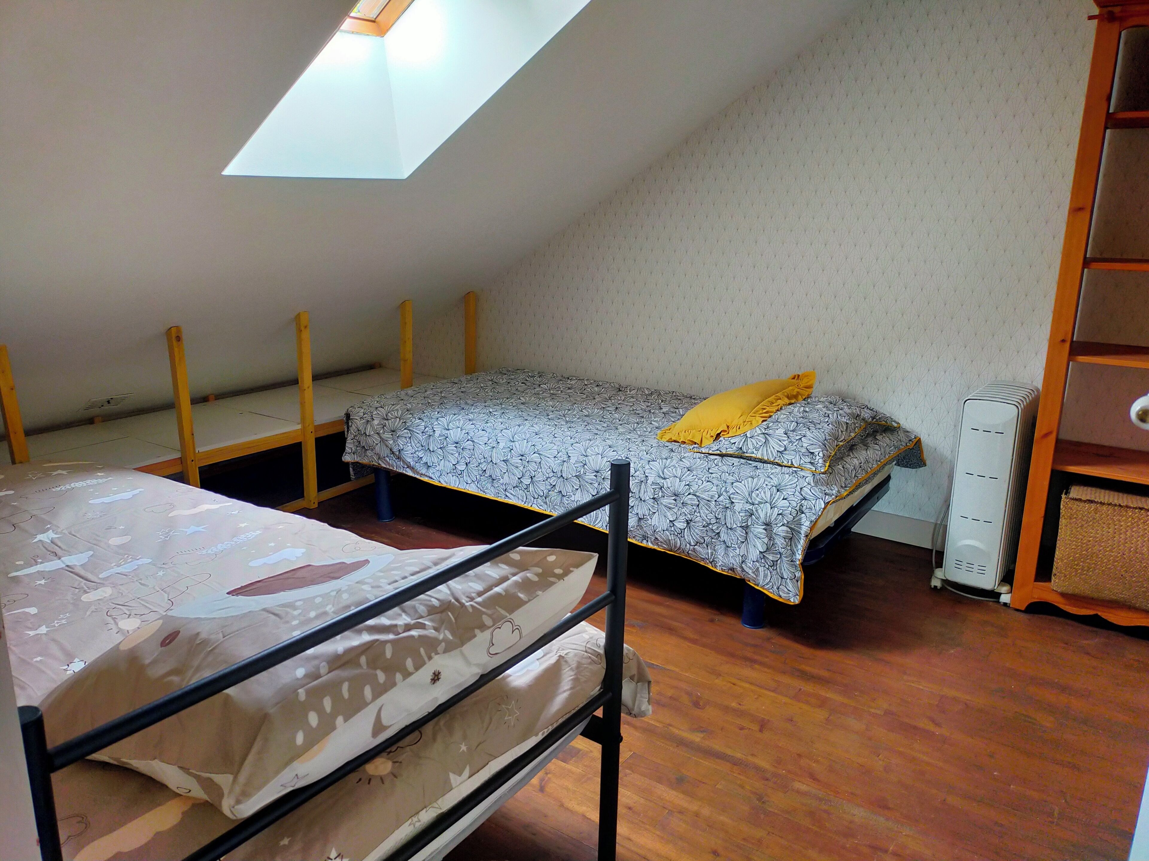 A dormitory room with bunk beds, a skylight, and a wooden dresser.