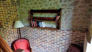 Une pièce chaleureuse avec un mur en briques, une bibliothèque en bois, un fauteuil rouge et un petit tabouret en bois.